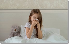 Sick child is sick at home, lying in bed with a teddy bear and blowing his nose in a handkerchief. The sad look of the girl. flu, acute respiratory viral infections, colds. Selective focus.
