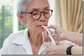 Nurse or caregiver taking care of disabled senior grandmother gives drinking water,feeding water using a straw to prevent choking and  difficulty or discomfort in swallowing,dysphagia in the elderly