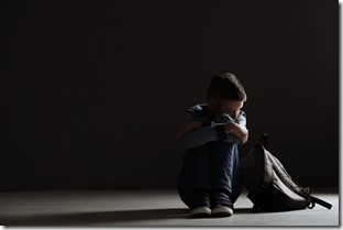 Upset boy with backpack sitting in dark room. Space for text