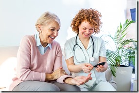 Happy senior woman having her blood sugar measured in a nursing home by her caregiver. Happy nurse measuring blood sugar of a senior woman in living room - diabetes and glicemia concept