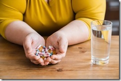 Fat plus size obese young woman sadly eating pills for losing weight in the kitchen. Healthy dieting concept, medicine for burning fat and calories