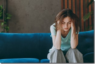 Young frustrated ill woman she 20s wear casual clothes mint t-shirt holding head suffer from headache close eyes sit on blue sofa indoor rest at home in own room apartment. People lifestyle concept