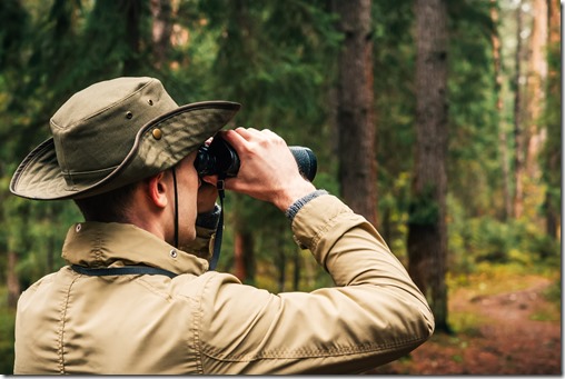 A man in a hat and uniform green and beige holds binoculars and looks into the distance, Ranger watching the territory, the protection of the reserve