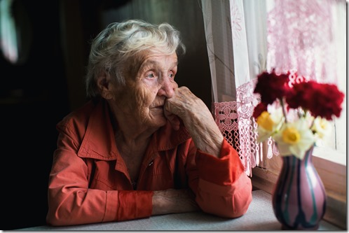 Elderly woman looks sadly out the window.