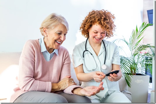 Happy senior woman having her blood sugar measured in a nursing home by her caregiver. Happy nurse measuring blood sugar of a senior woman in living room - diabetes and glicemia concept