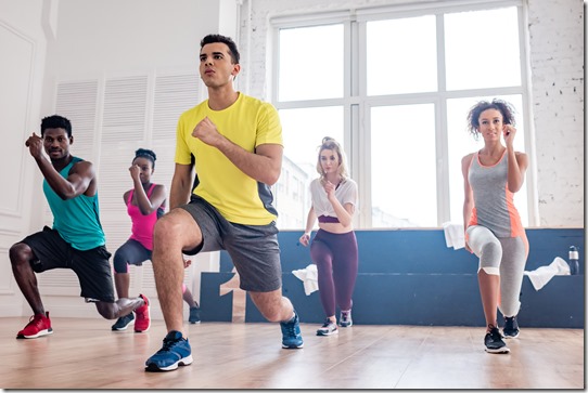 Low angle view of handsome trainer performing zumba with multiethnic dancers in dance studio